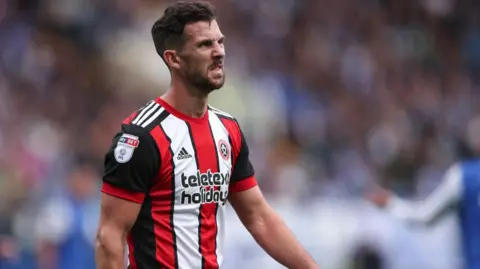 Getty Images A footballer in action on the pitch. He is wearing a red and white striped football shirt.