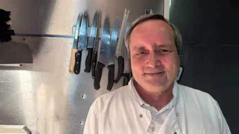 A man with dark grey hair smiles at the camera