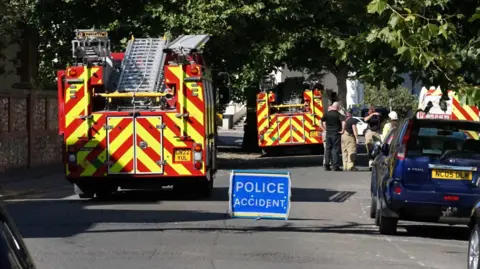 The image shows fire engines and a small blue sign that says "POLICE INCIDENT".