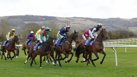 Reuters A group of jockeys riding racehorses around a track at Cheltenham racecourse.