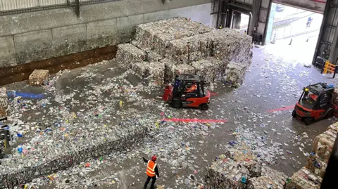 Two forklift trucks move huge bundles of rubbish in a big warehouse