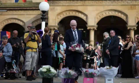 PA Media Southport MP Patrick Hurley lays flowers at a memorial to the victims of the Southport attack