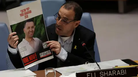 Reuters Released hostage Eli Sharabi holds up a photo of his brother Yossi Sharabi at the UN headquarters in New York (20 March 2025)