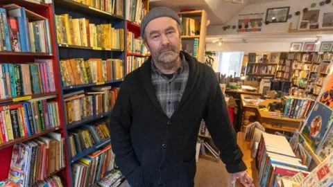 Bearded Paul Hamer with grey beanie hat, black and grey checked shirt, black cardigan.