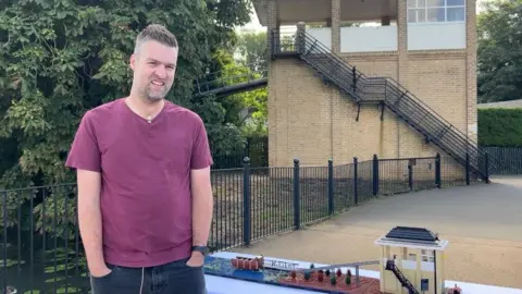 Wicksteed Park Rob Smith with short fair hair stands next to his model with the chute in the background