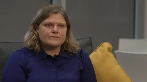 Councillor Grace Williams, a woman with shoulder-length light hair and wearing a dark blue shirt, sat on a grey sofa with a yellow cushion to the right