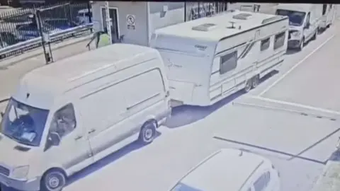 White vans towing caravans going through an opened barrier 