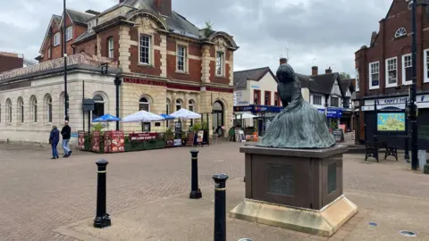 A picture of Nuneaton town centre with a statue of a writer George Elliot in the middle surrounded by brick and stone buildings