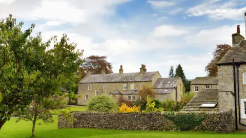 Getty Images A grass field with a stone wall adjoined to a Georgian-style stone built house with white window frames