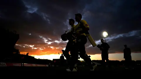 Getty Images Essex and Gloucestershire players leave the pitch in Bristol in the sunset with the floodlights bright