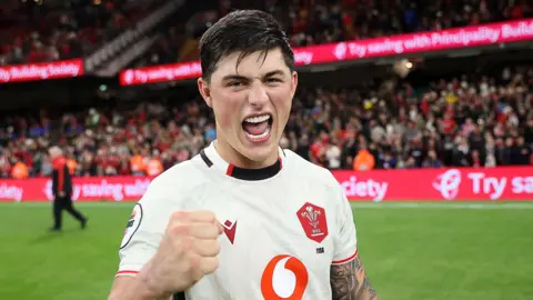 Louis Rees-Zammit pumps his fist in celebration for Wales while standing on the pitch