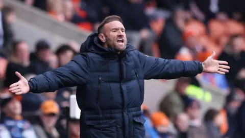 Blackpool boss Ian Evatt gesticulating with his arms out wide from his technical area, appealing against a decision which has gone against his side.