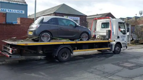 West Midlands Police A white truck with a trailer has a black small car on the back and is parked in an industrial area