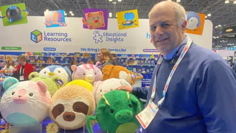 A man poses in front of a display of stuffed animals.