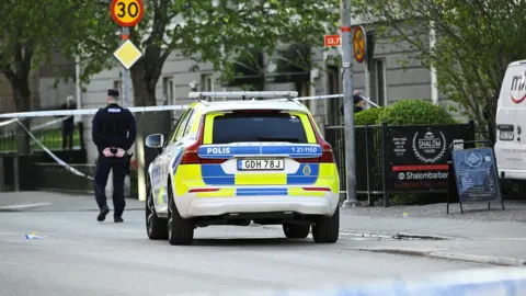 A police officer and police car next to a cordon at the scene of the shooting