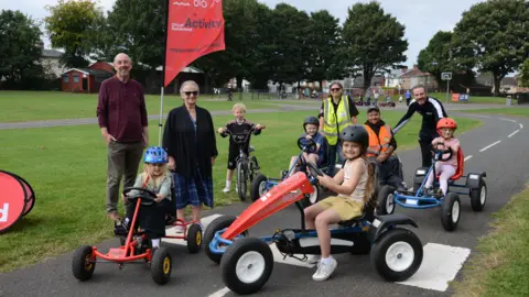 Houghton councillors John Price and Juliana Heron with youngsters from the Gateway Wheelers at the opening of the new Places to Ride learn to ride cycling track in Rectory Park, Houghton. The children are riding karts and bicycles.