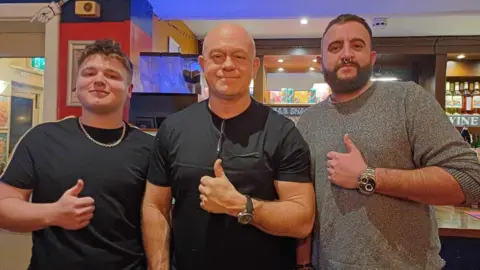 Jackie Henson Dan Mason with Ross Kemp and another man. He is wearing a black t shirt.