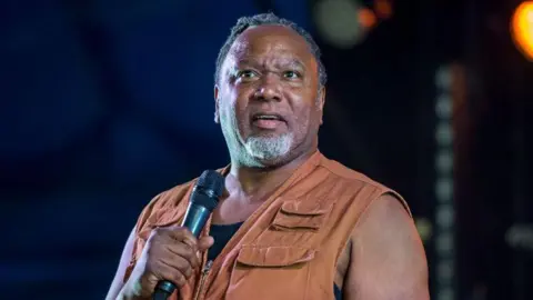Getty Images Reginald D Hunter performing at the Reading Festival in 2021. He is wearing a tan-coloured waistcoat.
