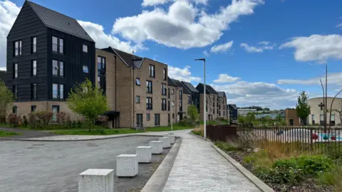 A view of a street, with several new build blocks of flats lining one end of the street, and a church visible in the distance