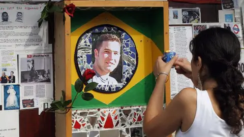 Getty Images A woman with her back to the camera lights a candle in front of a shrine which features a photo of Jean Charles at the centre of a painted depiction of the Brazilian flag. 