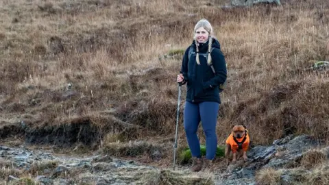 Stuart Smith Jennie hiking up a hill, with a little dog by her side.