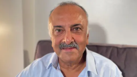 Mr Solanki has a moustache and is wearing a blue shirt