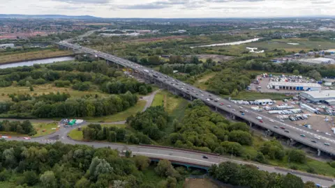 Getty Images A six-lane flyover runs from bottom right to top left through a wooded landscape and across a river.