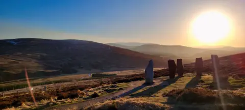 Hazel Thomson Four sculptural seats casting shadows on the ground with mountains behind them.