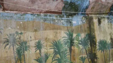 LDRS An old wall, looking dirty and damp with a fading and damaged mural of palm trees