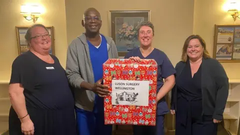Gill Harrison Four people with a donation box at Luson Surgery for the Christmas Sparkle Project