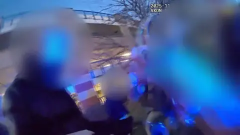 Essex Police A screen shot from a police body-worn camera. It is dark and the individuals being stopped by the police have their faces blurred out. Handcuffs can be seen being raised in the centre of the shot.