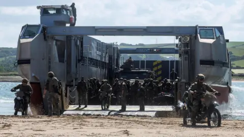 Royal Navy Troops and vehicles moving off a large landing craft on a beach