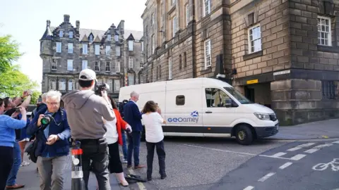PA Media A white van outside a stone building, with photographers crowding around it 