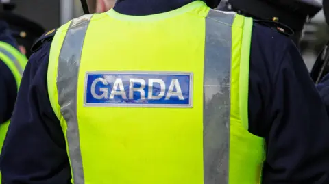 Getty Images A yellow illuminous vest has the words 'Garda' on it in silver font with a blue background.