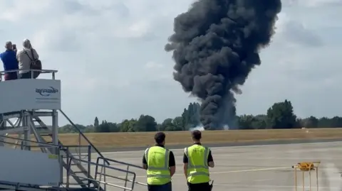 Four people look on as black smoke comes from the crashed plane in Southend