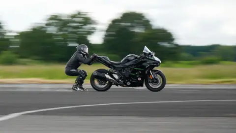 Alex Fowkes Jonny Davies in a helmet and black motorcycle gear being dragged behind a motorbike at a world record attempt test