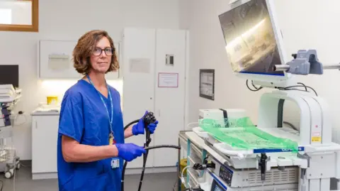 Kian Swainston A doctor wearing blue scrubs standing in an endoscopy theatre