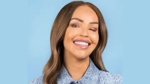 Katie Piper smiling at the camera, a blue background and she is wearing blue tweed. She has long brown hair.