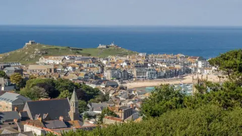 A seaside town with a tower in the foreground and buildings around a harbour with the sea in the background.