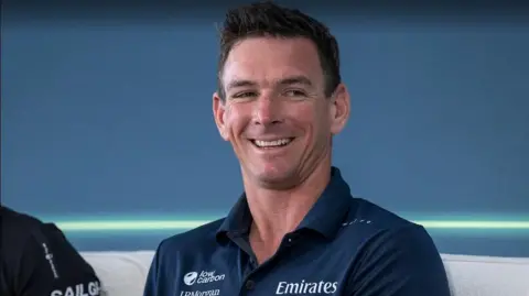 A man in a navy polo smiles looks off to the right of the camera.