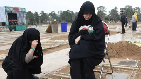 Two women crouch at the grave of a relative in a cemetary in Tehran on 16 March