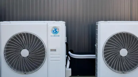 FILIP SINGER/EPA/Shutterstock Two brilliant white air conditioning units sit alongside each other outside a building. The only thing you see behind them are the corrugated steel oanels of the building itself.