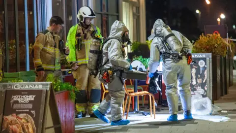 Emergency workers in protective suits and breathing gear carrying items outside Las Iguanas restaurant in Cardiff Bay 