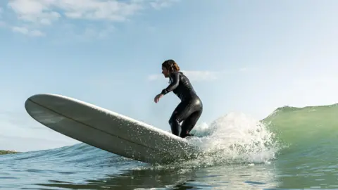 Carys Griffiths Laura Truelove surfing a longboard on an unbroken wave. 