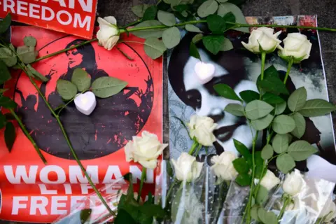 Getty Images Images of Mahsa Amini with flowers laid by them/