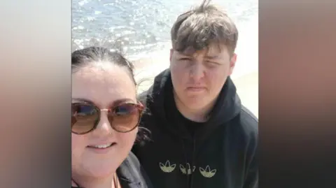 Marrissa Mullans has sunglasses, tied back brown hair and a black top. Her teenage Alfie is photographed with light brown hair and is wearing a black hoodie.