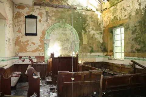 RCAHMW Interior view of chapel with paint peeling off the walls and its wooden pews and pulpit partly broken and in disarray and covered in crumbling plaster