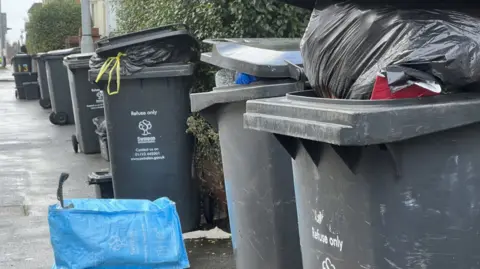 Overflowing black wheelie bins on a residential street in Swindon during last year's waste backlog