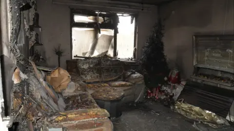 WMFS A living room, severely damaged by smoke and fire with burnt out sofas, a Christmas tree and blackened walls