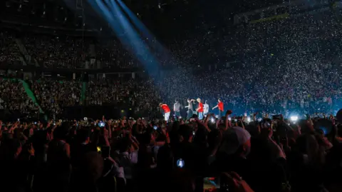 A banda K-pop do Beleft Lab aumentou no centro do palco mostrando milhares de fãs na arena assistindo-os.